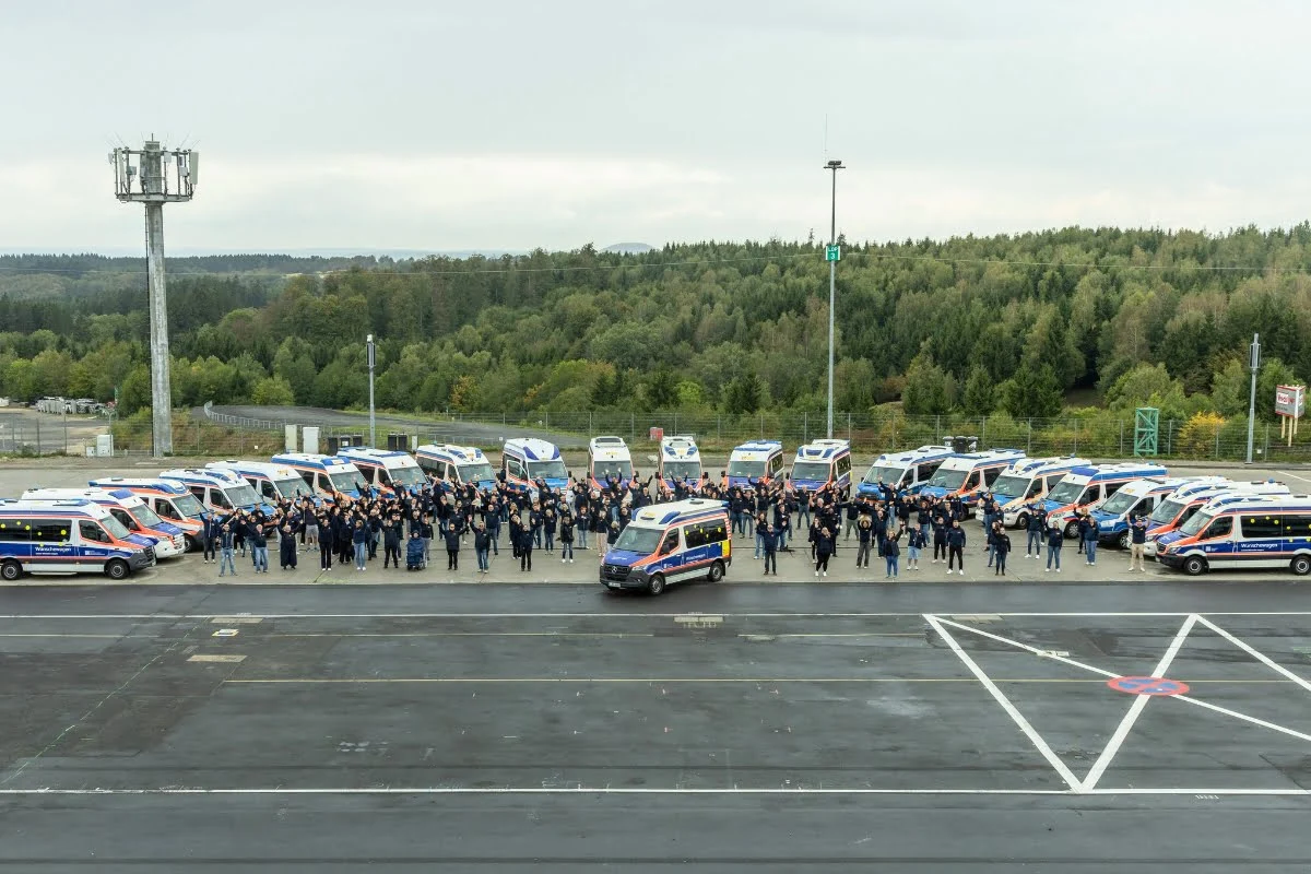 Ehrenamtliche und hauptamtliche Wunscherfüllen:innen von 21 ASB-Wünschwagenstandorten trafen sich im September 2026 zum Netzwerktreffen am Nürburgring. In der Mitte besonders gut zu sehen ist der ASB-Wünschewagen in seinem neuen Außendesign.